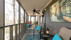 A covered porch with a ceiling fan, chairs, a table, a patterned rug, and a wall-mounted lantern.