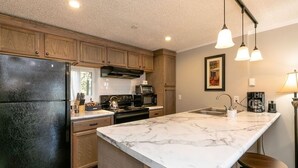 A kitchen with wooden cabinets, a black refrigerator, a marble island, and pendant lighting.