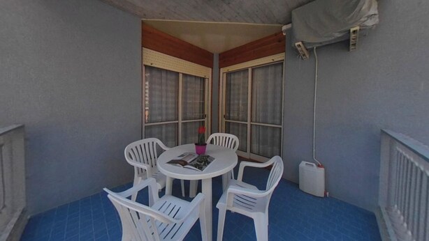 A small balcony with a round table and four white plastic chairs, a potted plant, and a ceiling fan. - Beachfront Family Flat With Terrace (Lignano Sabbiadoro)