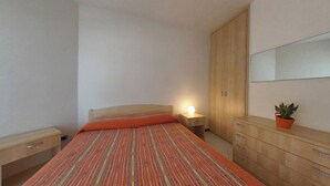 A bedroom with a bed, bedside table, nightstand, wardrobe, and a potted plant. - Beachfront Family Flat With Terrace (Lignano Sabbiadoro)