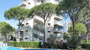 A multi-story building with balconies, a swimming pool, and surrounding greenery. - Beachfront Family Flat With Terrace (Lignano Sabbiadoro)