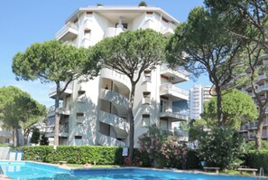 A multi-story building with balconies, a swimming pool, and surrounding greenery. - Beachfront Family Flat With Terrace (Lignano Sabbiadoro)