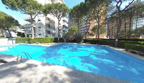 A swimming pool with a diving board, surrounded by trees and multi-story buildings. - Beachfront Family Flat With Terrace (Lignano Sabbiadoro)