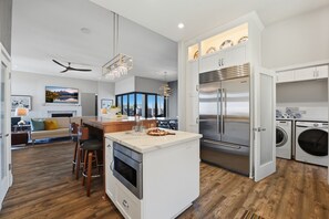 A modern kitchen with a central island, built-in appliances, and a dining area with a view. - Limited July Availability | Luxury Pacific Beach Retreat with Pool, Spa & Endles (San Diego)