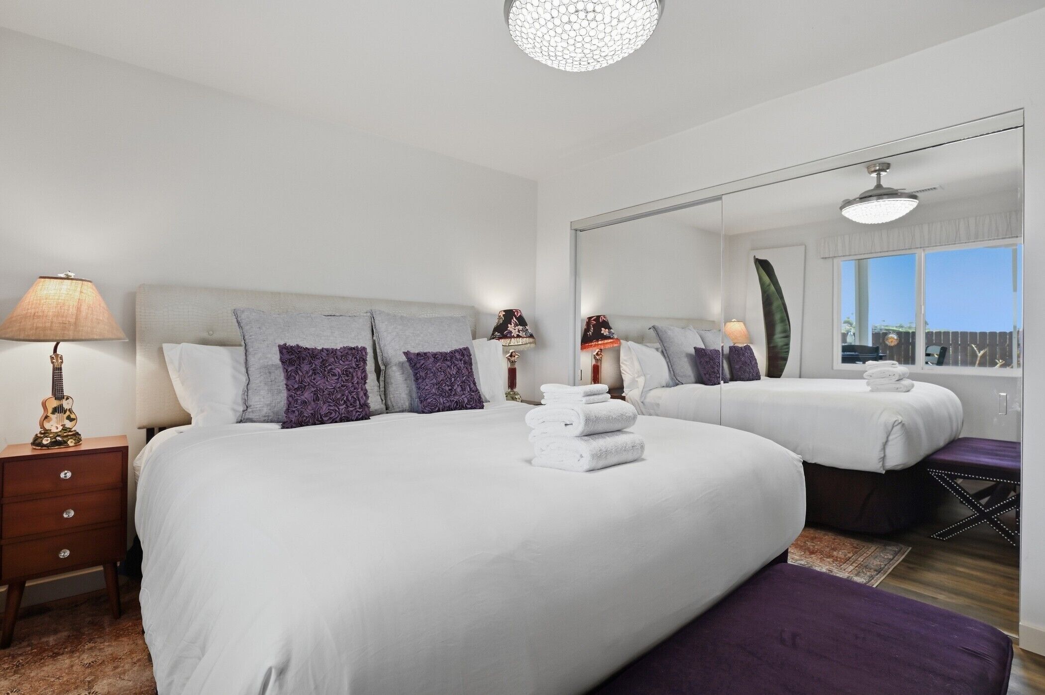 A hotel room with two beds, a large mirror, a nightstand with a lamp, and a view of the outside.