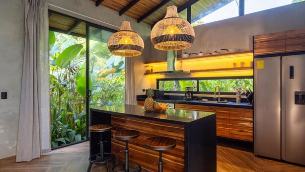 A modern kitchen with a central island, bar stools, and a large window with a view of greenery.