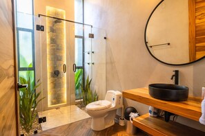 A modern bathroom with a glass-enclosed shower, a toilet, and a wooden vanity with a black basin.