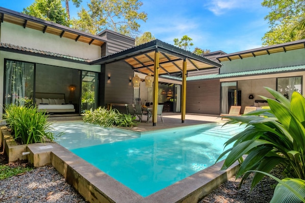 A modern house with a swimming pool, outdoor seating, and a covered patio area.