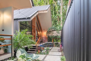 Ein modernes Haus mit einer Treppe, die zu einer Holzterrasse inmitten üppiger Vegetation führt.