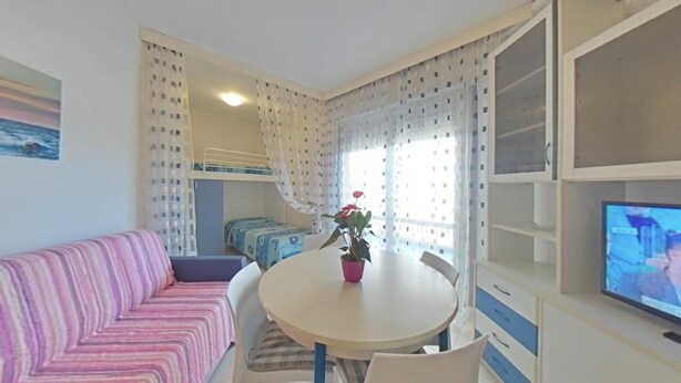 Ein Zimmer mit Etagenbetten, einem runden Tisch mit Stühlen, einem Fernseher und einer Zimmerpflanze.