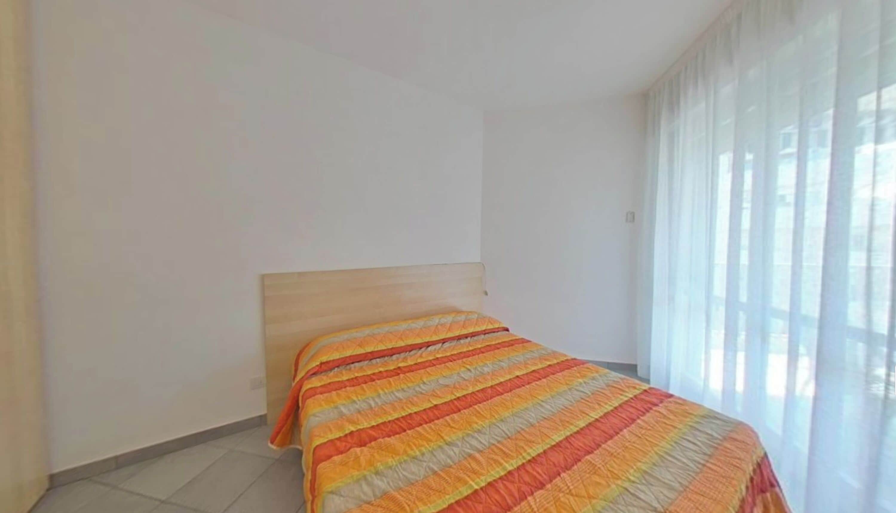 A room with a bed, a window with curtains, and a plain wall.