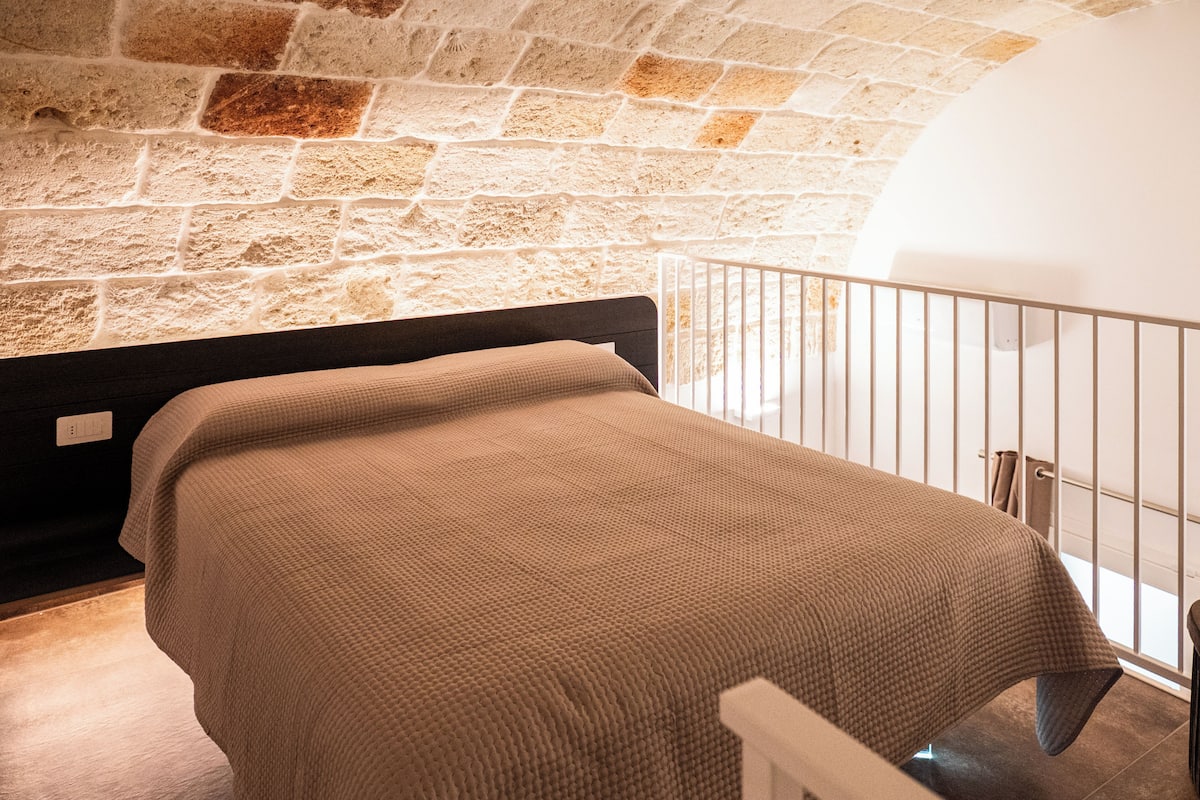 A room with a bed, a stone wall, and a white railing.