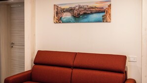 A room with a red sofa, a painting of a coastal scene, and a white door. - Pachita Seaside Rooms (Polignano a Mare)