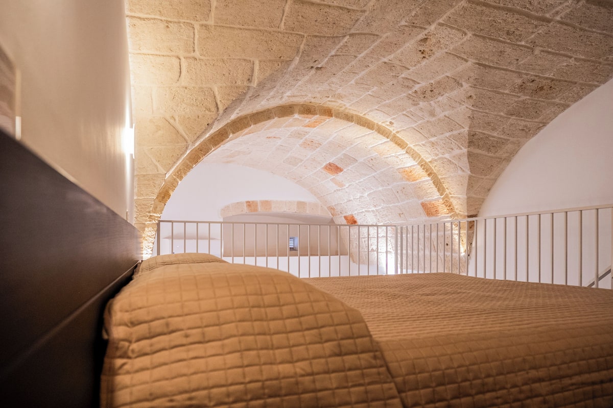 A room with a brick ceiling, a bed with a quilted blanket, and a white railing.