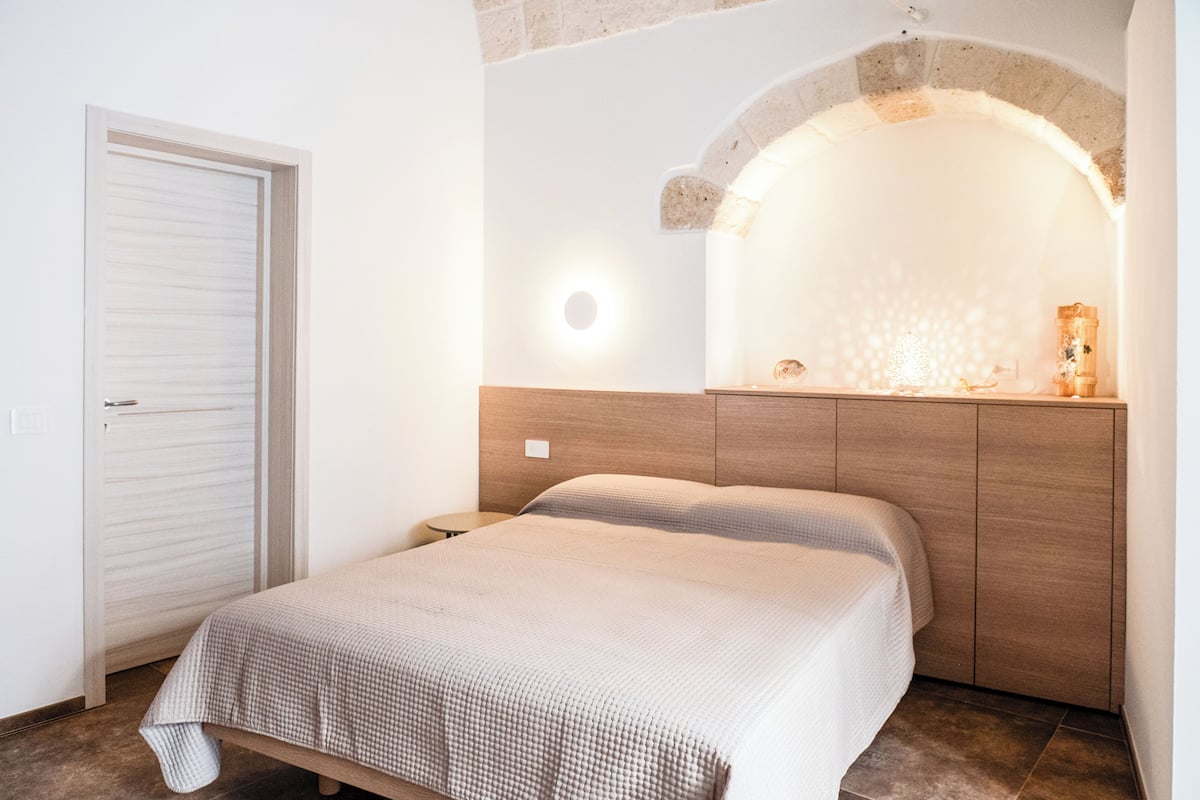 A bedroom with a bed, a nightstand, a wardrobe, and a stone archway.