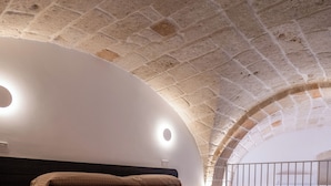 A room with a stone ceiling, a bed with a headboard, and a circular light fixture. - Pachita Seaside Rooms (Polignano a Mare)