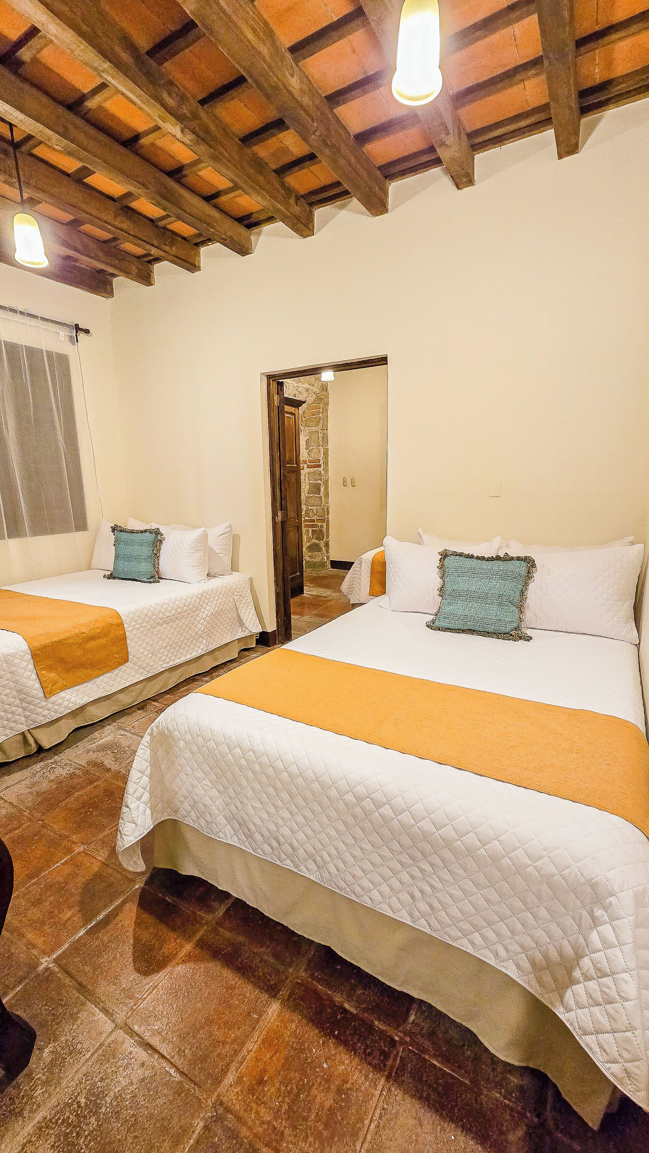 A room with two beds, a stone wall, and a wooden ceiling.