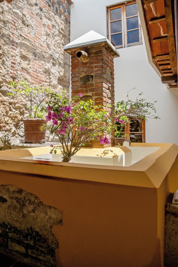 A courtyard with a brick tower, potted plants, and a wooden bench. - Hotel Casa Colonial by AHS (Antigua Guatemala)