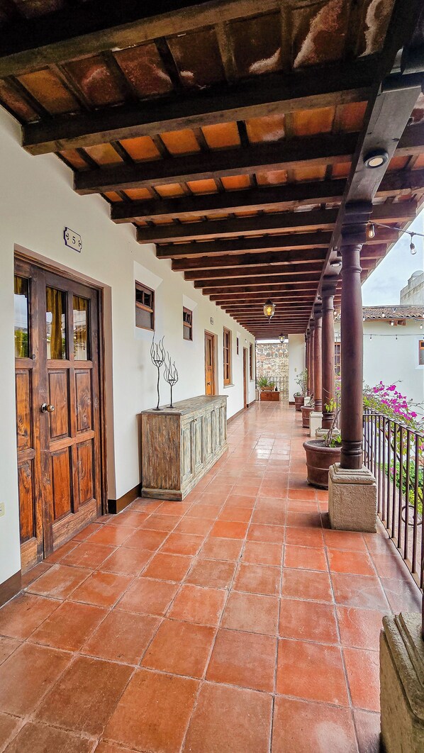 Un corredor cubierto con piso de baldosas, puertas de madera y columnas.