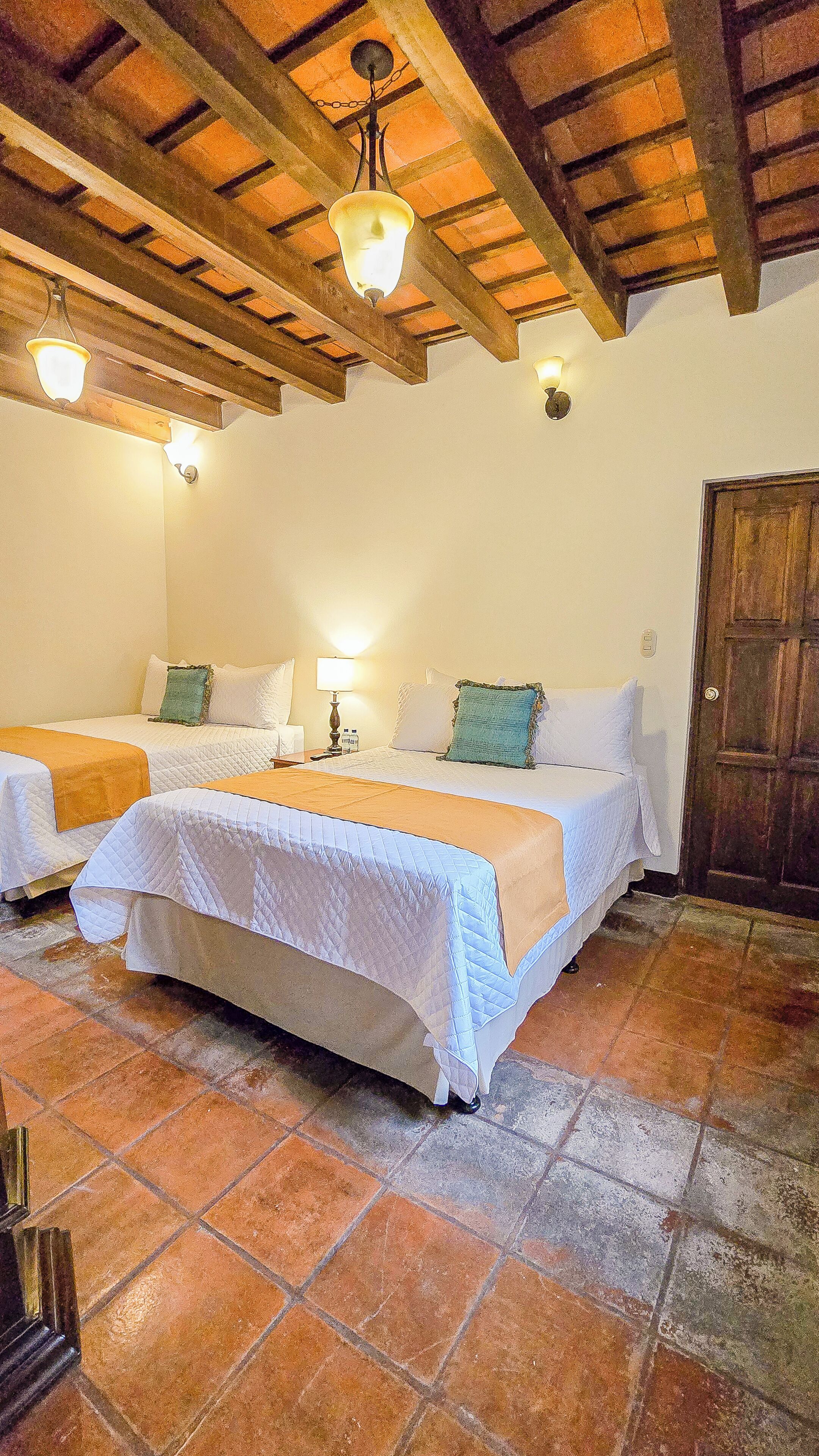 A room with two beds, a wooden ceiling, and a tiled floor.