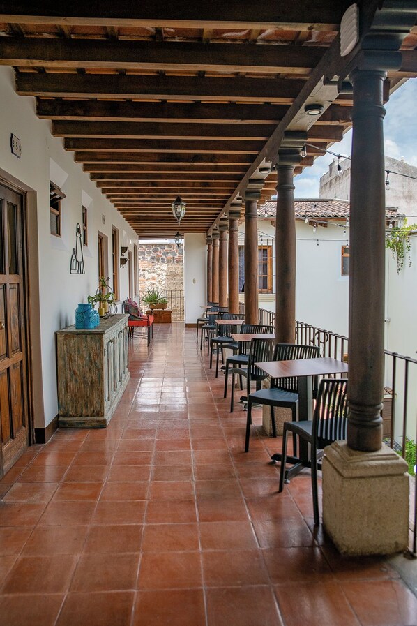 A covered outdoor seating area with wooden beams, tiled flooring, and tables and chairs. - Hotel Casa Colonial by AHS (Antigua Guatemala)