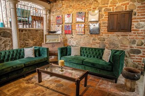 Una habitación con dos sofás tapizados en verde, una mesa de centro y una pared de piedra con obras de arte.