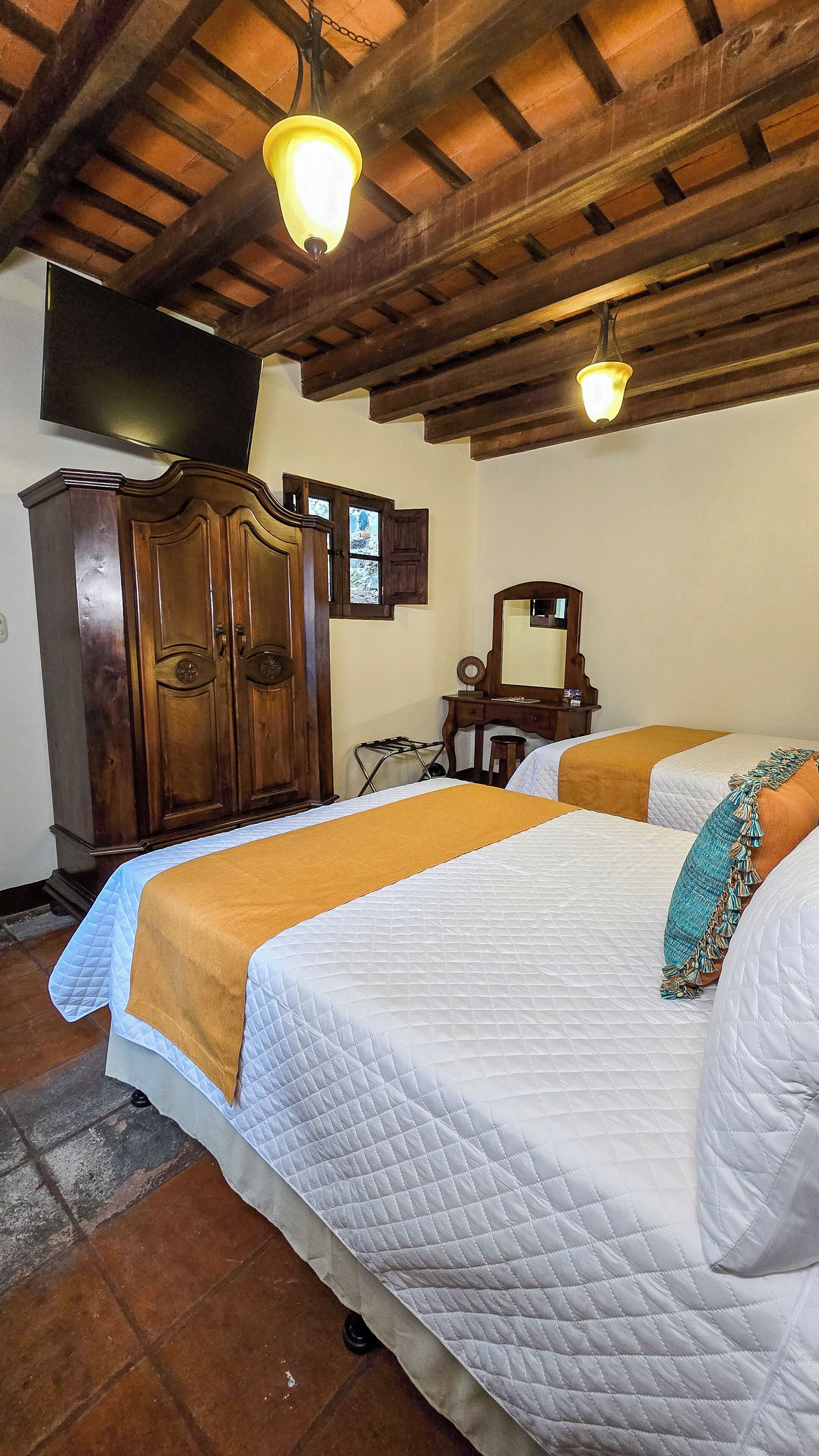 Habitación con dos camas, muebles de madera, televisión y piso de baldosas.