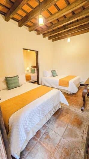 A room with three beds, each with a white quilt and a green pillow. There is a wooden ceiling with exposed beams and a hanging light fixture. - Hotel Casa Colonial by AHS (Antigua Guatemala)