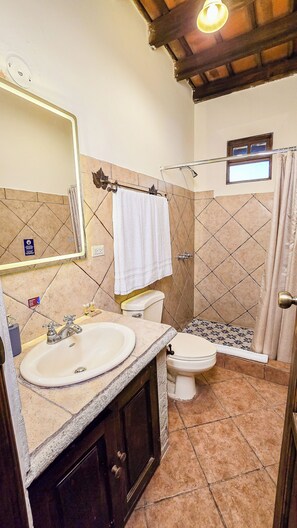 A bathroom with a sink, toilet, and shower. There is a mirror above the sink, and a towel hanging on a rack. - Hotel Casa Colonial by AHS (Antigua Guatemala)
