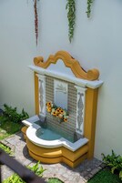 Una pequeña fuente con una parte superior decorativa, rodeada por un muro con diseño y una base amarilla.