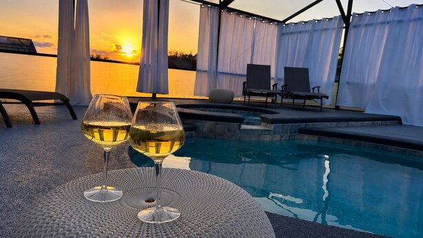A poolside area with two glasses of white wine, a pool, and a sunset view. - The Sanctuary (Davenport)