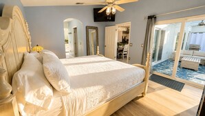 A large bed with a headboard, a ceiling fan, and a view of a balcony with a sofa. - The Sanctuary (Davenport)