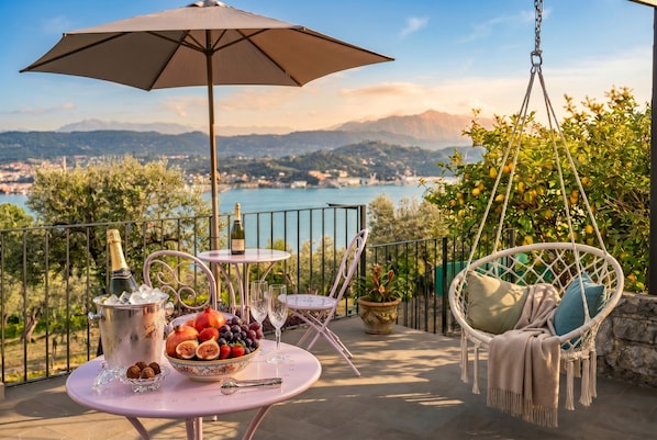 Una terraza con una mesa lista para una comida, un sillón colgante y vistas a un lago y montañas.