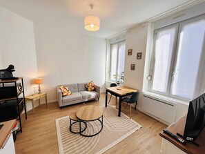 Een moderne woonkamer met een bank, een ronde salontafel, een eettafel, een televisie en een lamp.