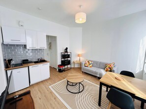 A compact living space with a kitchenette, a dining area, and a sofa with colorful cushions. - La Suite des Bleuets - Centre-ville (Reims)