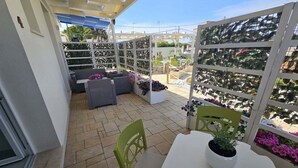 Eine Terrasse mit Sitzgelegenheiten im Freien, einem weißen Tisch mit einem Blumentopf und einem weißen Trennwerk mit einer Pflanzenanordnung.