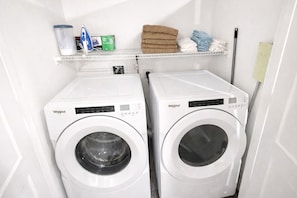 A laundry room with two Whirlpool front-loading washing machines, a shelf with towels and cleaning supplies, and a mop. - Luxury 2BR and 2BA Uptown CLT Retreat ;Walk to BOA Stadium & City Hotspots  (Charlotte)