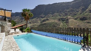 Ein Pool mit Holzzaun, Steinboden und Blick auf Berge.