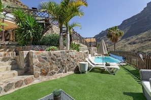 A pool area with artificial grass, lounge chairs, and a stone wall. - Vacation Home 'Arguineguín Retreat' with Mountain View, Wi-Fi and Air Conditioning (San Bartolomé de Tirajana)
