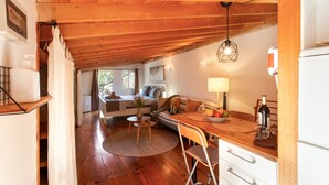 Ein gemütliches Zimmer mit Holzbalkendecke, einem Esstisch mit Stühlen, einer Couch und einer Lampe.