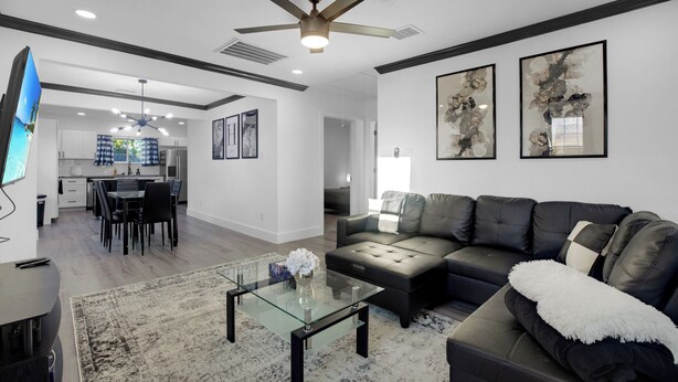 A modern living room with a glass coffee table, a black leather sofa, and a dining area with a kitchen in the background.