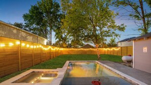A backyard with a swimming pool, wooden fence, and string lights.