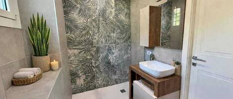 Un baño con un espejo grande, un lavamanos, una planta en maceta y una pared con diseño de hojas.