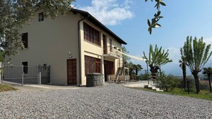 A two-story building with a gravel driveway, a gated entrance, and a balcony with outdoor seating. - ThreeZeroThree House • With Private Garden (Colombaro)