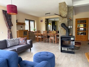 A living room with a sofa, ottoman, dining table, chairs, a fireplace, and a kitchen area visible through an open door.