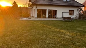 Ett hus med ett sluttande tak, stora fönster och en gräsig trädgård.
