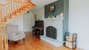 Una sala de estar con una escalera de madera, una chimenea, un piano y un sillón cómodo.