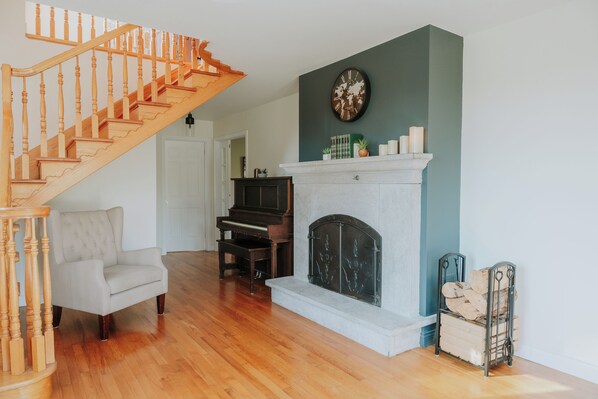 Una sala de estar con una escalera de madera, una chimenea, un piano y un sillón cómodo.