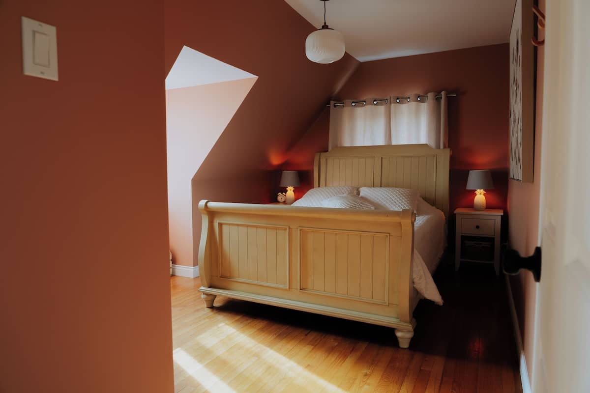 A bedroom with a wooden bed, a nightstand with a lamp, and a sloped ceiling.