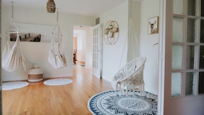 A room with a wooden floor, a round patterned rug, macrame hanging chairs, a woven basket, and a hanging light fixture.
